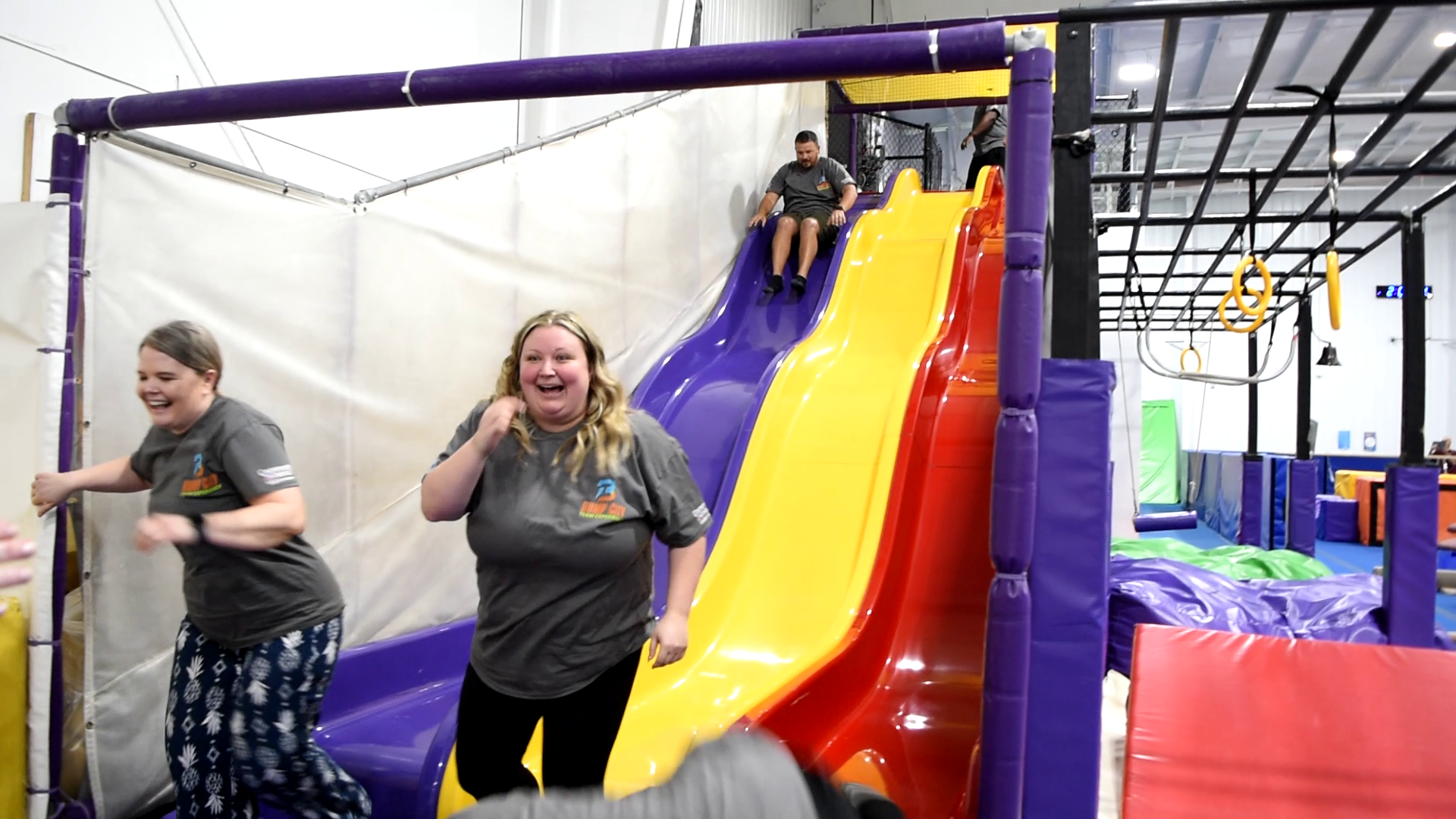 Team members laughing while going down the indoor slide at Bump City